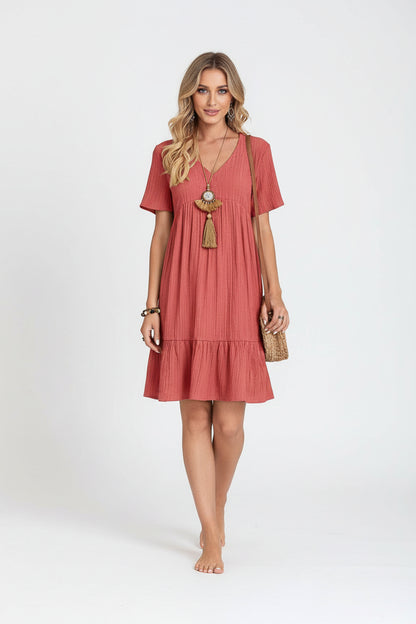 Woman wearing a red dress holding a straw bag against a plain background