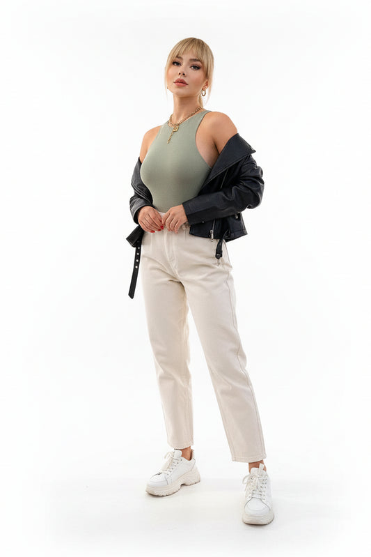 Woman posing against a light-colored wall wearing a green top and white pants.