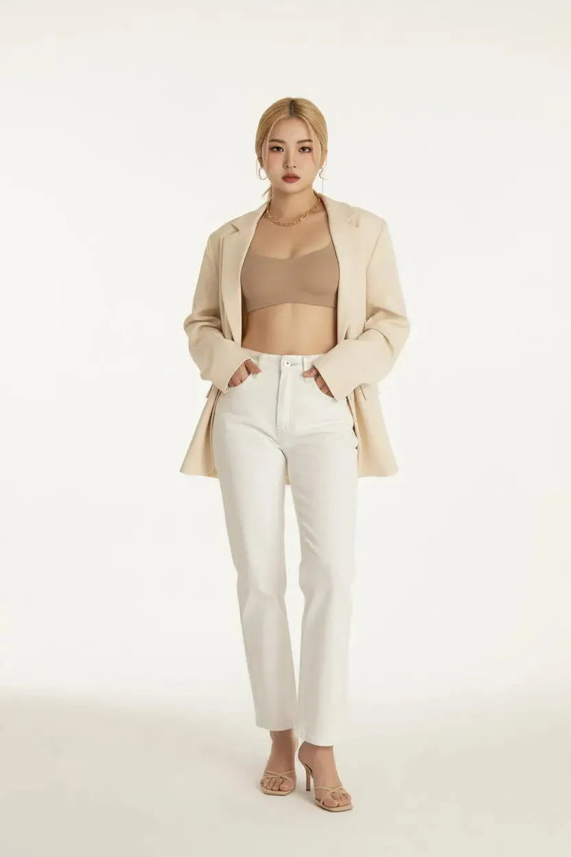 Person wearing a beige bralette and white pants with a neutral background