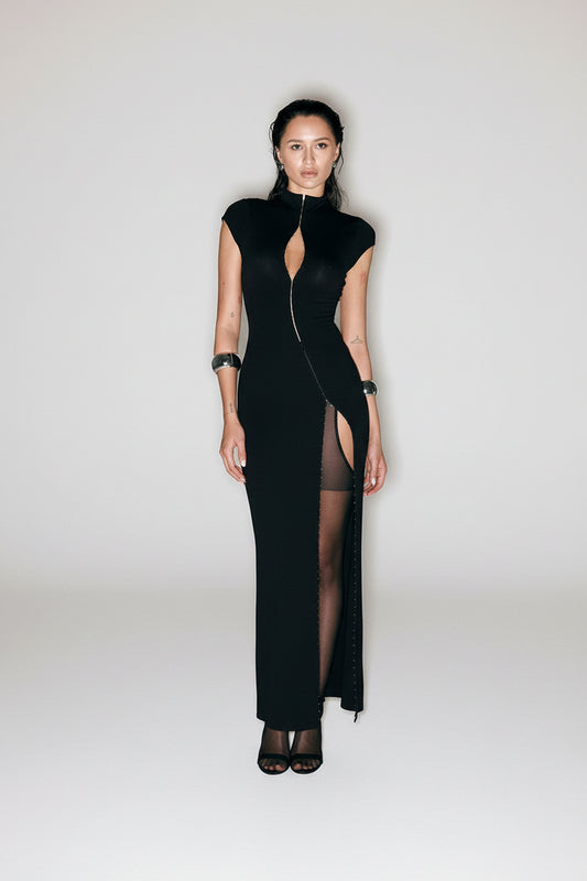 Woman wearing a black dress with a high slit on a plain background